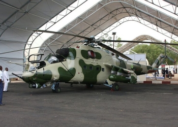 An Mi-24 V attack helicopter its in an open hanger. The Mi-24 “V” variant is distinguishable by its rotary gun turret.